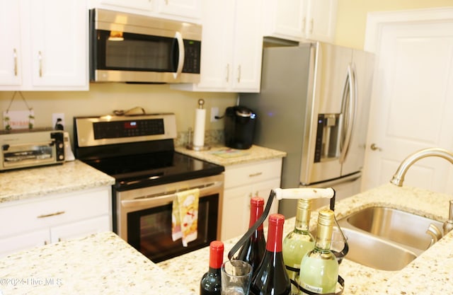 kitchen with sink, white cabinetry, light stone counters, and stainless steel appliances