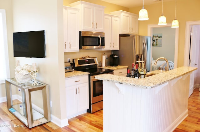 kitchen with a kitchen breakfast bar, hanging light fixtures, stainless steel appliances, light wood-type flooring, and white cabinets