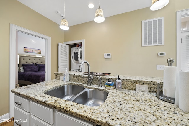 kitchen with stacked washer / dryer, light stone countertops, sink, and hanging light fixtures