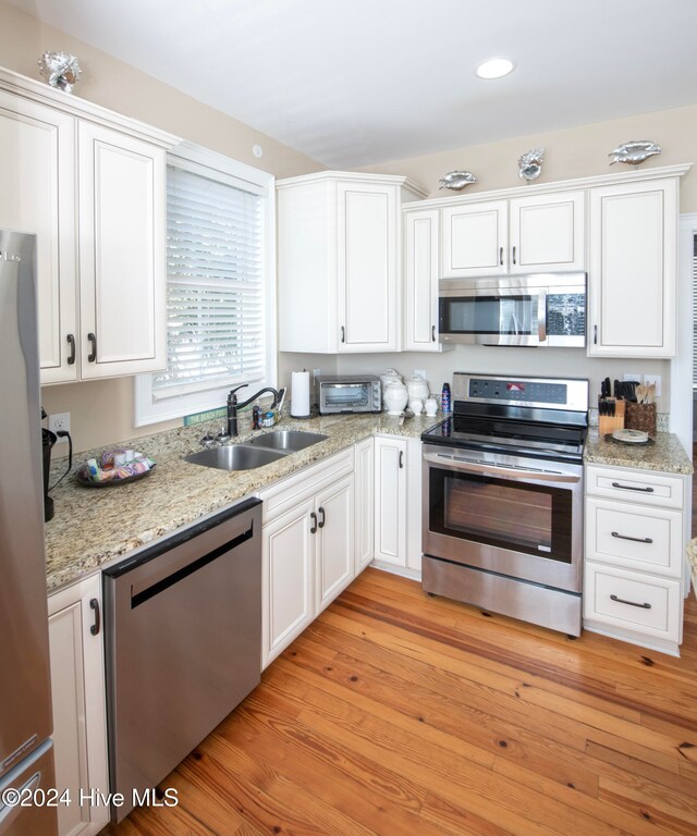 kitchen with stainless steel appliances, sink, light stone countertops, light wood-type flooring, and white cabinetry