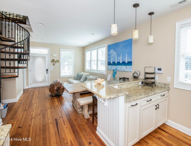 kitchen featuring light hardwood / wood-style floors, kitchen peninsula, white cabinets, and light stone countertops