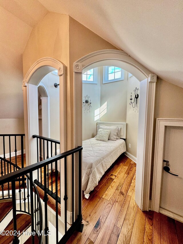 bedroom with a textured ceiling, wood-type flooring, and vaulted ceiling