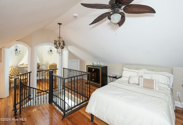 bedroom with lofted ceiling, hardwood / wood-style floors, and ceiling fan with notable chandelier