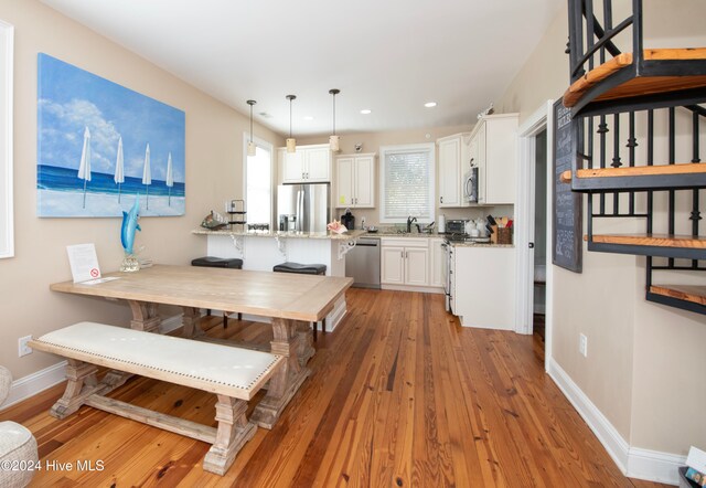 kitchen featuring kitchen peninsula, appliances with stainless steel finishes, a kitchen breakfast bar, white cabinetry, and wood-type flooring