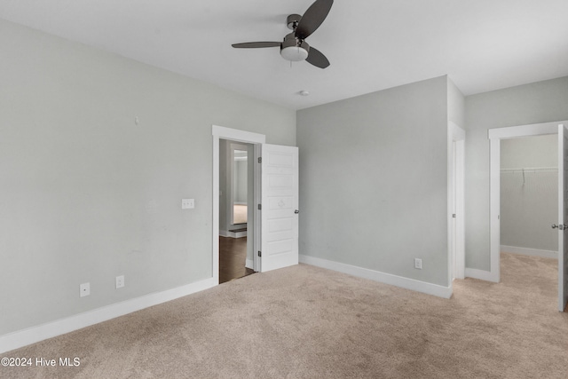 unfurnished bedroom with a walk in closet, a closet, ceiling fan, and light colored carpet