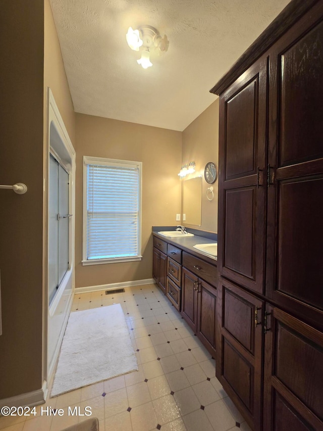 bathroom featuring vanity, bath / shower combo with glass door, and a textured ceiling