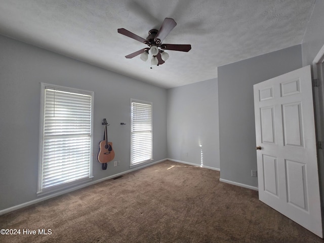 unfurnished room with ceiling fan, a textured ceiling, and dark carpet