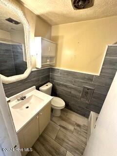 bathroom featuring vanity, toilet, and tile walls