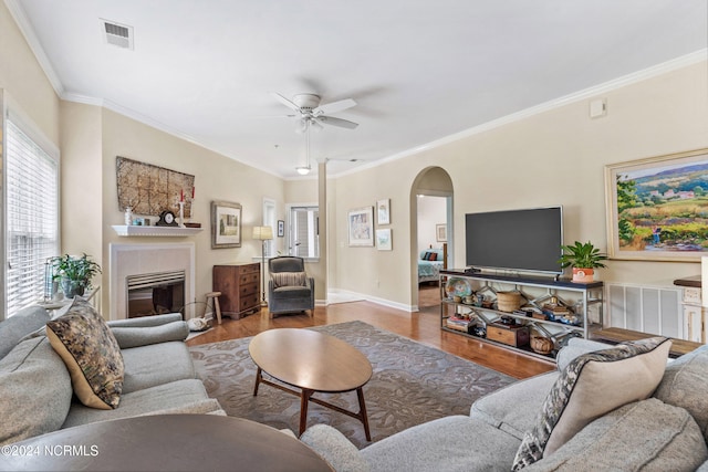 living room featuring hardwood / wood-style flooring, a tile fireplace, crown molding, and ceiling fan