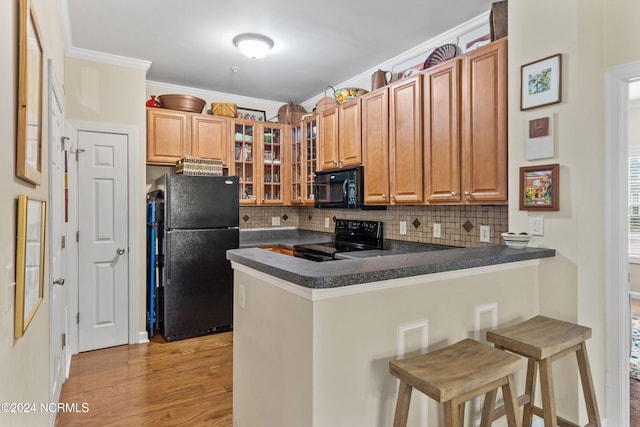 kitchen featuring black appliances, crown molding, decorative backsplash, kitchen peninsula, and a breakfast bar