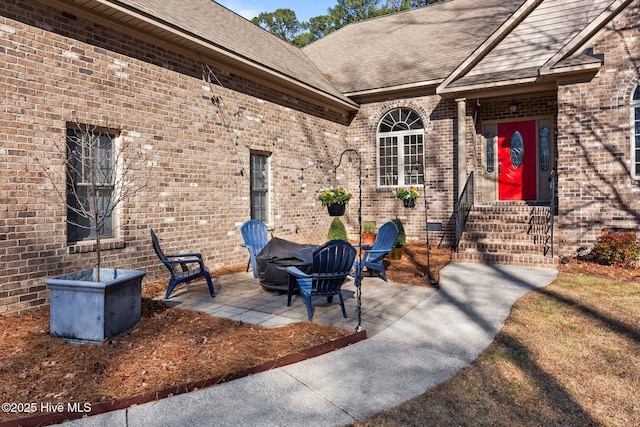 entrance to property featuring crawl space, a patio area, a shingled roof, and brick siding