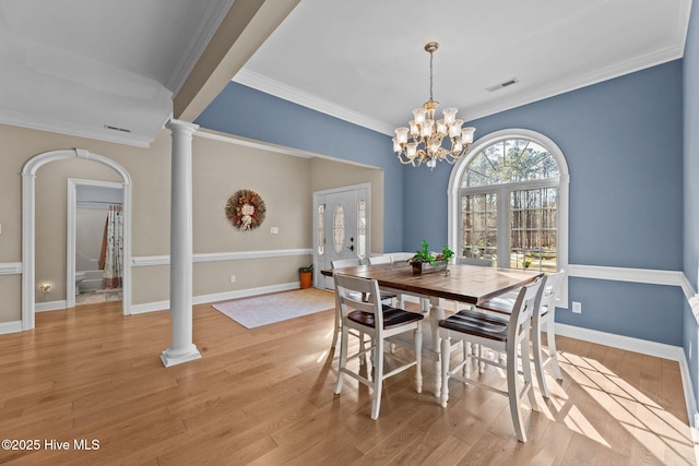 dining area with light wood-type flooring, decorative columns, an inviting chandelier, and crown molding