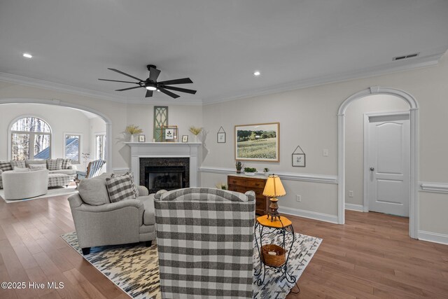 living area featuring light wood-type flooring, arched walkways, a fireplace, and ornamental molding