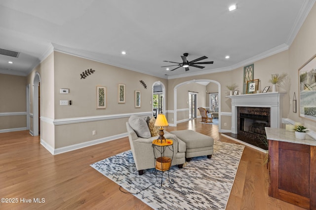 living room featuring crown molding, a high end fireplace, light wood-type flooring, and ceiling fan