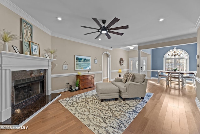 living room with ceiling fan with notable chandelier, crown molding, a high end fireplace, and light hardwood / wood-style flooring