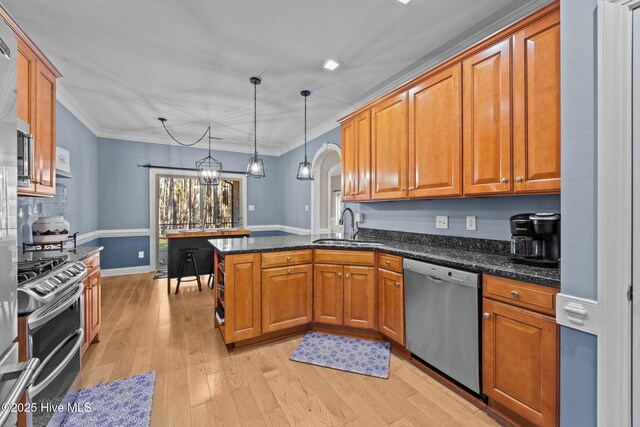 kitchen with stainless steel appliances, a sink, brown cabinets, dark stone countertops, and decorative light fixtures