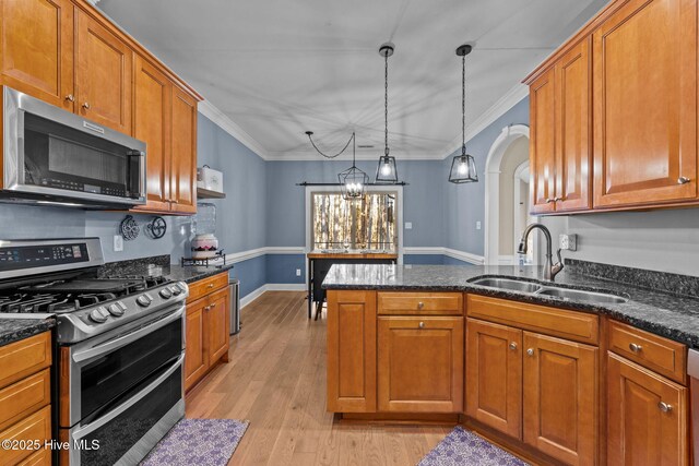 kitchen with arched walkways, hanging light fixtures, appliances with stainless steel finishes, a sink, and a peninsula