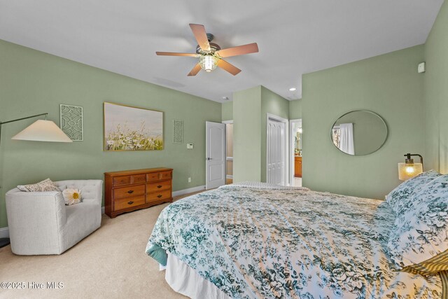 bedroom with a ceiling fan, light colored carpet, ensuite bath, and baseboards