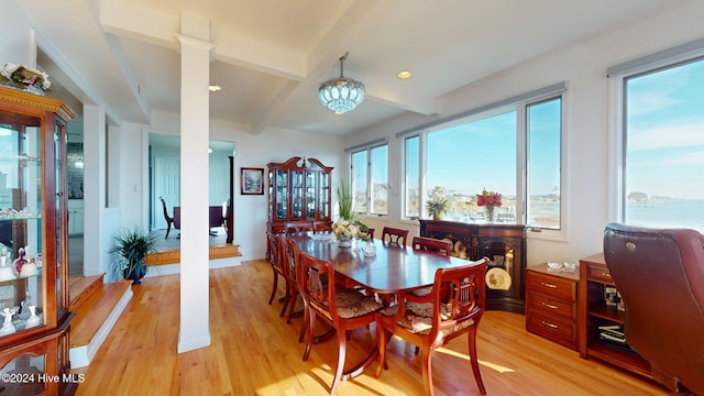 dining area with light hardwood / wood-style floors, a water view, beam ceiling, and a chandelier