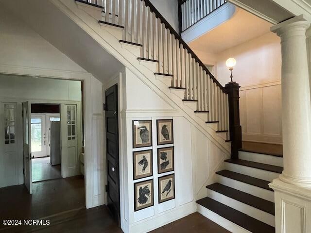 stairway with ornate columns, wood-type flooring, and a high ceiling