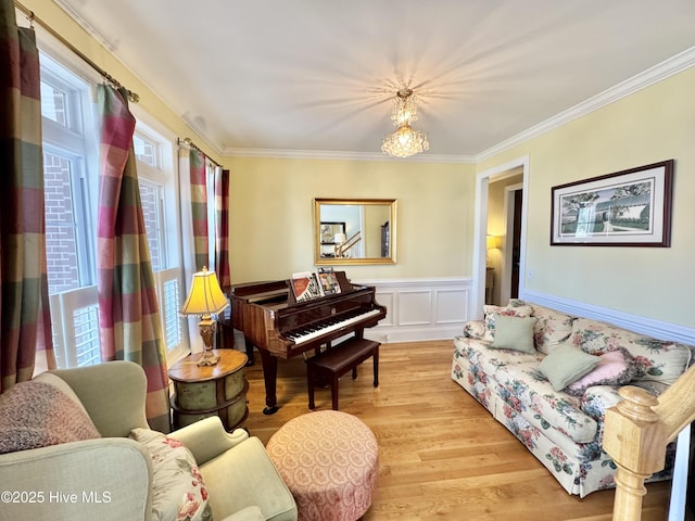 living area featuring a decorative wall, ornamental molding, wainscoting, light wood-style floors, and a notable chandelier