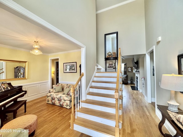 stairway with a chandelier, a wainscoted wall, wood finished floors, and ornamental molding