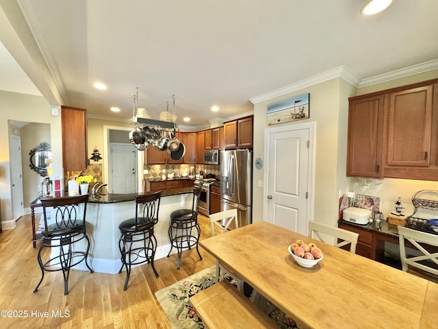 kitchen featuring backsplash, a kitchen bar, light wood-style flooring, a peninsula, and stainless steel appliances