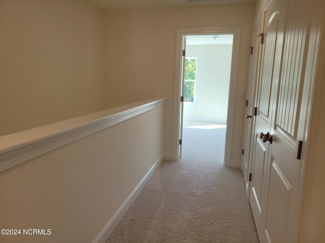 corridor featuring light colored carpet and baseboards