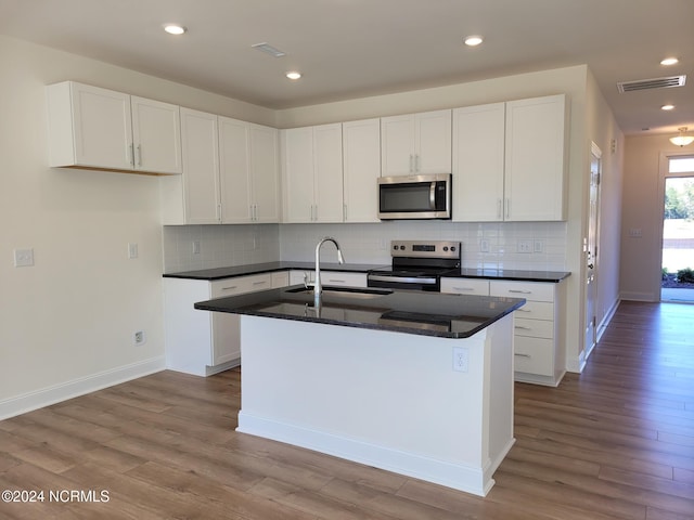kitchen with appliances with stainless steel finishes, a sink, wood finished floors, a center island with sink, and white cabinets