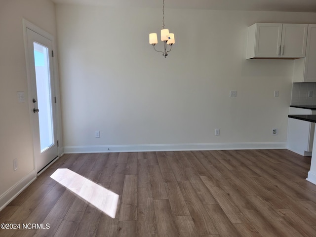 unfurnished dining area with a chandelier, wood finished floors, and baseboards
