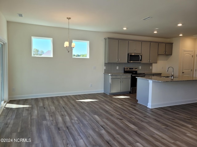 kitchen with appliances with stainless steel finishes, gray cabinetry, a sink, dark wood-style floors, and stone countertops