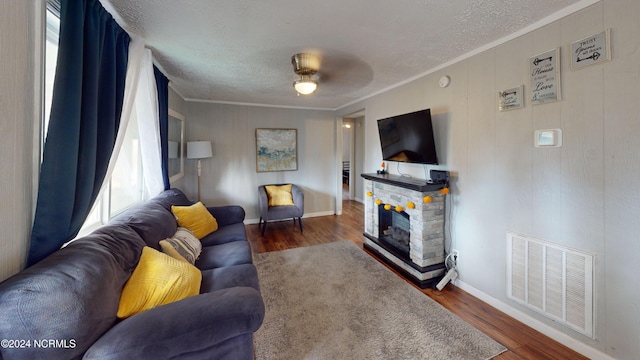 living room featuring a stone fireplace, ornamental molding, dark wood-type flooring, and ceiling fan