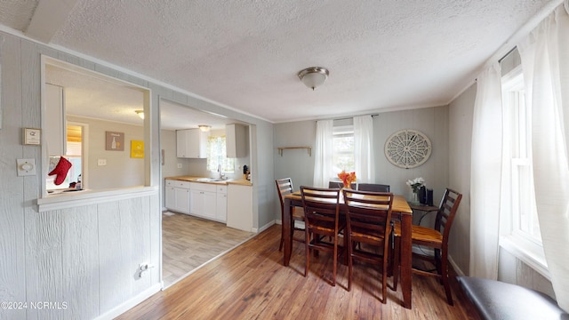 dining room featuring sink, crown molding, a textured ceiling, and light hardwood / wood-style flooring