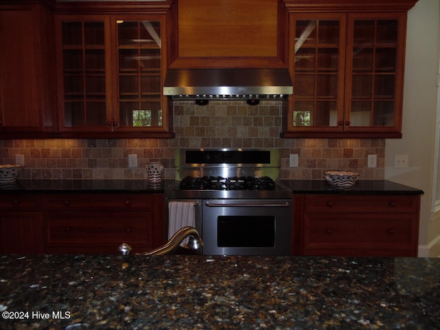 kitchen with wall chimney exhaust hood, dark stone countertops, stainless steel gas range, and tasteful backsplash