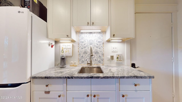 kitchen featuring light stone countertops, sink, white fridge, and white cabinets