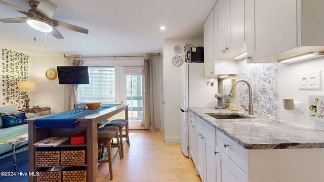 kitchen with light stone counters, sink, white cabinets, ceiling fan, and light hardwood / wood-style flooring