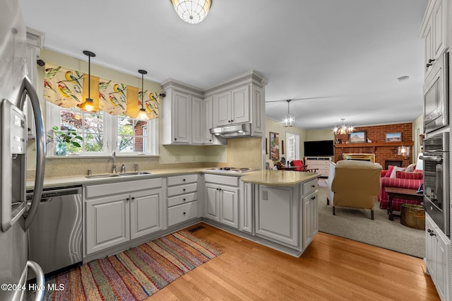 kitchen with stainless steel appliances, sink, a brick fireplace, pendant lighting, and light wood-type flooring