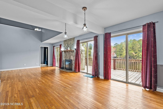 unfurnished living room with light hardwood / wood-style floors, a stone fireplace, and beamed ceiling