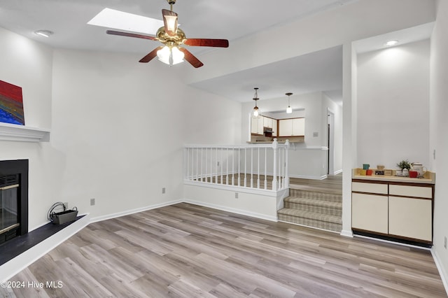 unfurnished living room featuring a skylight, light hardwood / wood-style flooring, and ceiling fan