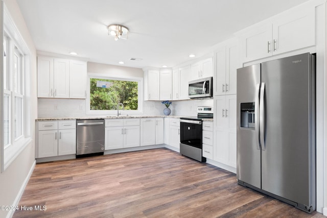 kitchen with dark hardwood / wood-style flooring, tasteful backsplash, light stone counters, stainless steel appliances, and white cabinetry