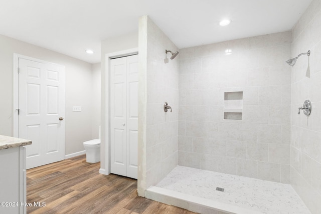 bathroom with a tile shower, hardwood / wood-style flooring, vanity, and toilet