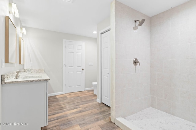 bathroom with a tile shower, vanity, toilet, and wood-type flooring