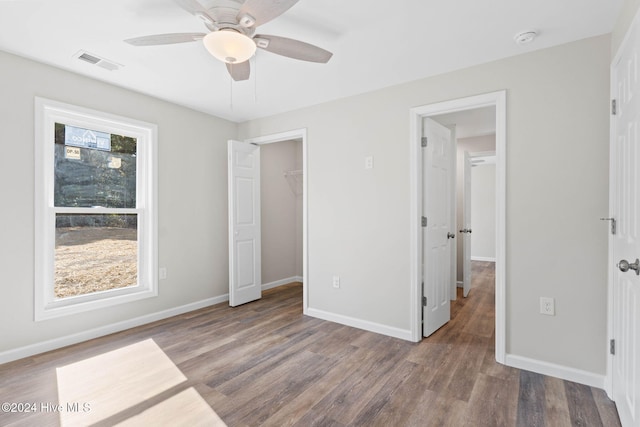 unfurnished bedroom with ceiling fan, wood-type flooring, a spacious closet, and a closet