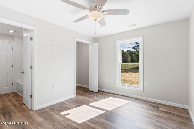 unfurnished bedroom featuring a spacious closet, ceiling fan, wood-type flooring, and a closet