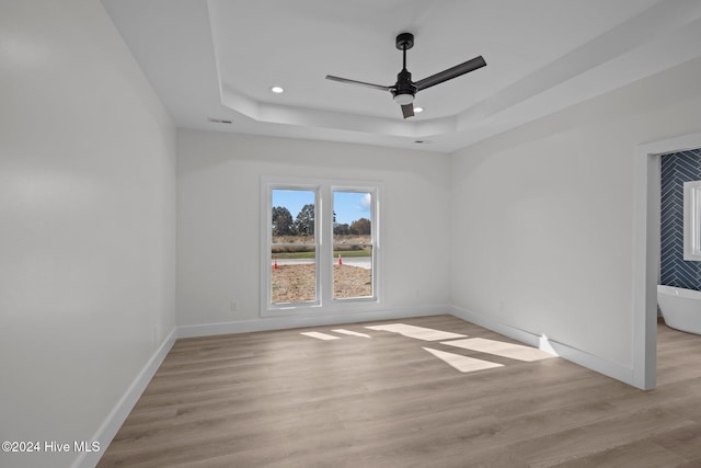 empty room featuring a raised ceiling, ceiling fan, and light hardwood / wood-style floors