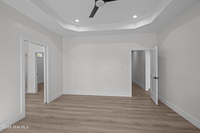 empty room featuring a raised ceiling, ceiling fan, and light hardwood / wood-style floors