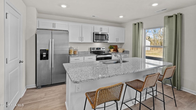 kitchen featuring appliances with stainless steel finishes, white cabinetry, an island with sink, sink, and light wood-type flooring