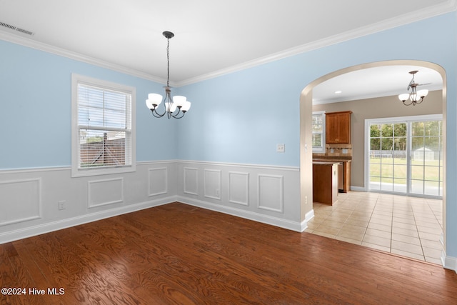 empty room with a notable chandelier, light wood-type flooring, and crown molding