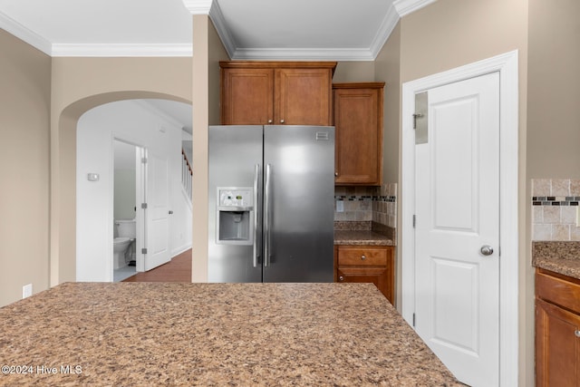 kitchen featuring light stone countertops, crown molding, decorative backsplash, and stainless steel refrigerator with ice dispenser