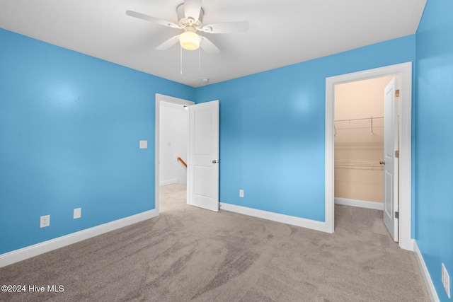 unfurnished bedroom featuring a walk in closet, a closet, light colored carpet, and ceiling fan